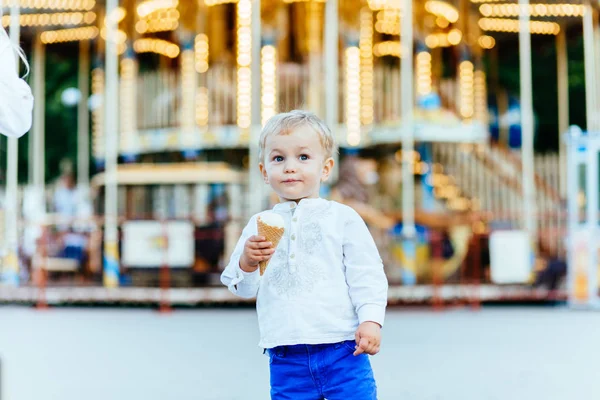 Batole chlapec jíst zmrzlinu nad pozadím s kolotoč v zábavním parku — Stock fotografie