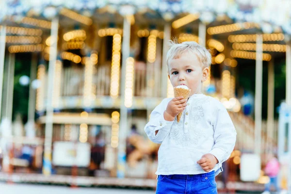 Komik yürümeye başlayan çocuk beyaz gömlek ve Mavi pantolon atlıkarınca önünde bir dondurma yemek