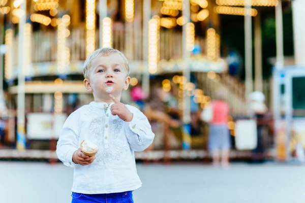 Funny batole boy v bílou košili a modré kalhoty zmrzlina před kolotoč — Stock fotografie