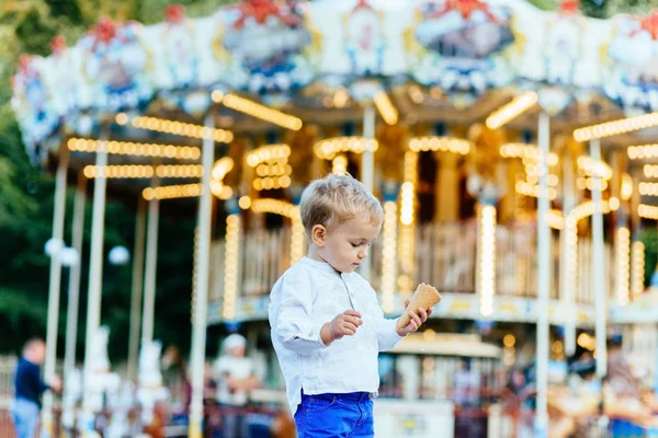 Komik yürümeye başlayan çocuk beyaz gömlek ve Mavi pantolon atlıkarınca önünde bir dondurma yemek