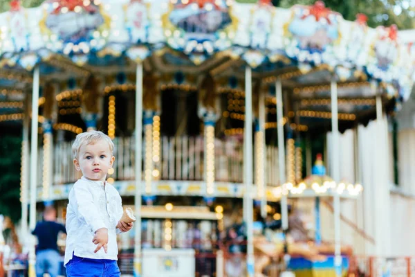Komik yürümeye başlayan çocuk beyaz gömlek ve Mavi pantolon atlıkarınca önünde bir dondurma yemek