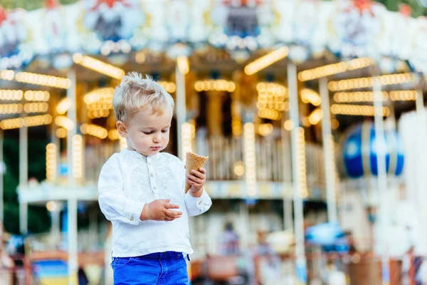 Funny batole boy v bílou košili a modré kalhoty zmrzlina před kolotoč — Stock fotografie