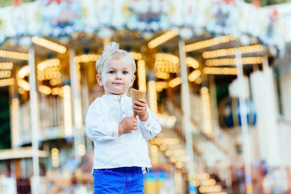 Komik yürümeye başlayan çocuk beyaz gömlek ve Mavi pantolon atlıkarınca önünde bir dondurma yemek