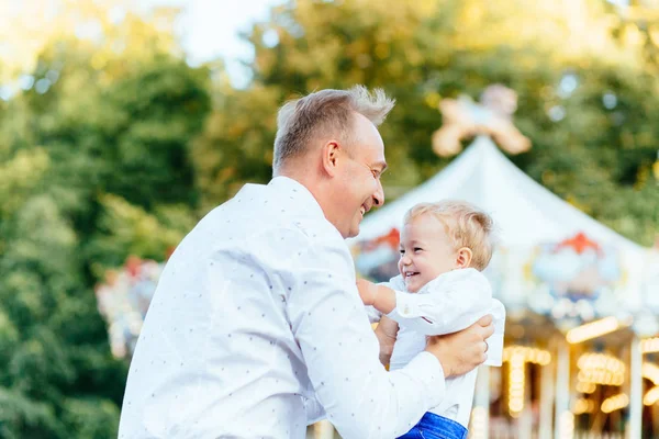 Счастливый отец бросает сына под кайф перед каруселью в парке развлечений — стоковое фото