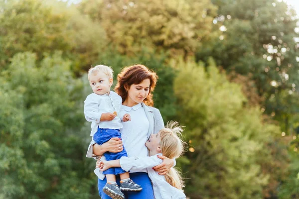 Felice madre sorridente con due bambini che si divertono insieme sullo sfondo dell'albero verde. Vacanze estive e concetto di famiglia . — Foto Stock