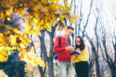 Kitap okuma, tek kullanımlık fincan kahve içme, sonbahar bir parkta konuşmak iki üniversite öğrencileri.