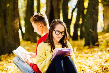 Bir park ve bir kitap okuma serisi fotoğraf güzel esmer kadın güneş gözlüğü ve kırmızı gömlekli arka arkaya düşmüş bir sonbahar üzerinde oturan genç adam bırakır