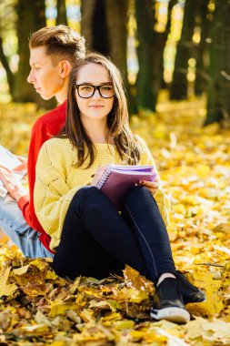 Bir park ve bir kitap okuma serisi fotoğraf güzel esmer kadın güneş gözlüğü ve kırmızı gömlekli arka arkaya düşmüş bir sonbahar üzerinde oturan genç adam bırakır