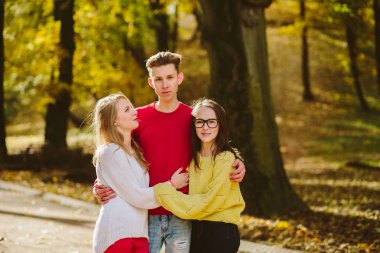 Bir takım üç mutlu arkadaşlar öğrencilerin hugs ve parkta gülüyor. Eğitim, yaşam tarzı ve insanlar kavramı.