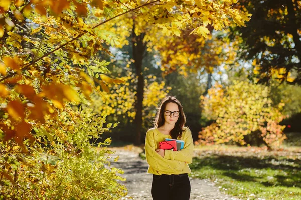美丽的学生女孩的肖像在秋季公园的书籍 成年女生享受教育 美丽的女性穿着黄色毛衣 围巾和眼镜 回到学校 — 图库照片