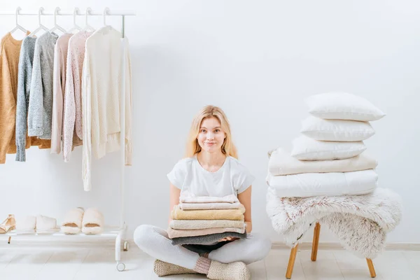 Junge Hausfrau auf dem Boden sitzend mit einem Stapel Kissen, Decke kariert auf weißen Wandstapelturm Design im skandinavischen Stil, Kleiderständer in modernem Licht leeren Kleiderschrank Raum. — Stockfoto