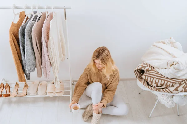 Jonge blonde positieve vrouw zit in haar licht moderne kleedkamer op de vloer en drinkt 's morgens koffie. Bovenaanzicht. Mode blog, website, social media held header sjabloon — Stockfoto