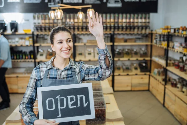 Female business owner holding OPEN sign in bakery