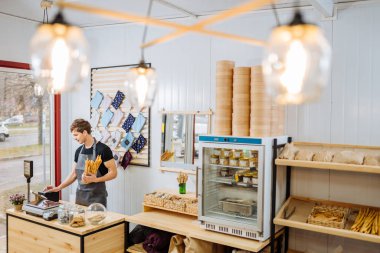 Küçük iş adamları ve hizmet kavramı. Küçük işletme sahibi dükkânda kasası olan mutlu bir erkek müşterinin siparişini notla kontrol ediyor. Önlüklü genç adam dükkanda çalışıyor..