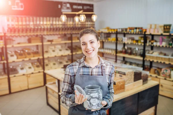 Proprietario di razza mista che vende superprodotti nel negozio Zero Waste Shop. Un sacco di cibo sano in bottiglie di vetro in stand nel negozio di alimentari. Nessun minimalismo cosciente di plastica Vegan Lifestyle Concept. Focus selettivo — Foto Stock