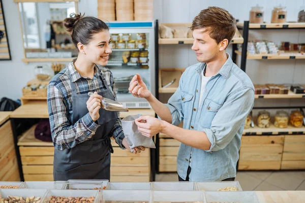 Giovane donna sorridente con un sacchetto di carta in mano sceglie le nocciole e le versa in un sacchetto . — Foto Stock