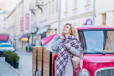 Sokakta poz veren güzel, mutlu bir kızın açık hava portresi. Kağıtları tutan, kameraya bakan, şık kıyafetler giyen bir manken. Kış tatili, Noel, Yeni Yıl konsepti.