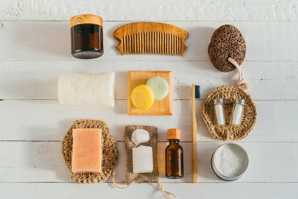 Zero waste bathroom accessories on blue background. Flat lay bamboo toothbrushes, wooden hair comb, handmade soap, massage brush, luffa sponge and green leaves. Natural organic SPA cosmetic products — Stock Photo, Image