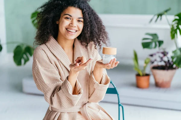 Retrato de mulher bonita sorrindo enquanto toma algum creme facial isolado no fundo branco com espaço de cópia — Fotografia de Stock