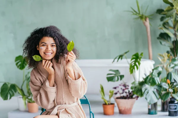 Retrato de belleza de una mujer juguetona en el baño cubriéndose los ojos con hojas de limonero en la mano con plantas verdes sobre el fondo. Cuidado de la piel, limpieza, eco, orgánico, cero residuos, reducir, reutilizar, reciclar . — Foto de Stock