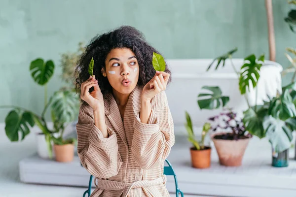 Portrait de beauté de femme ludique dans la salle de bain couvrant ses yeux avec des feuilles de citronnier à la main avec des plantes vertes sur le fond. Soin, nettoyage, éco, bio, zéro déchet, réduire, réutiliser, recycler . — Photo