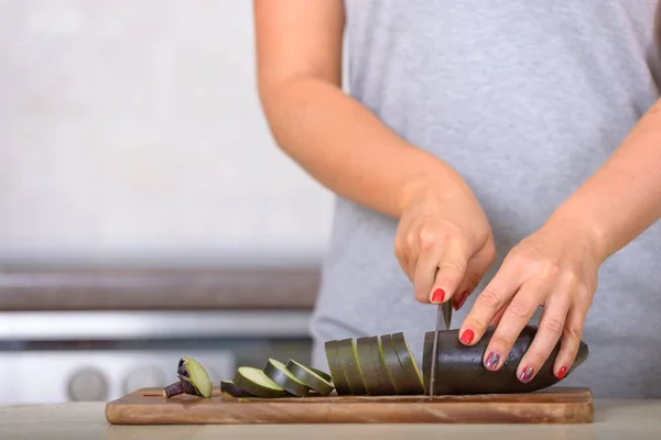 Mulher cortando beringela com uma faca na tábua de madeira — Fotografia de Stock