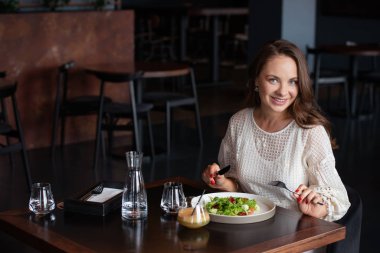 Gülümseyen kadın kafede vejetaryen salatası yiyor.