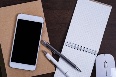 Akıllı telefon, not defteri ve kalemli ofis masası.