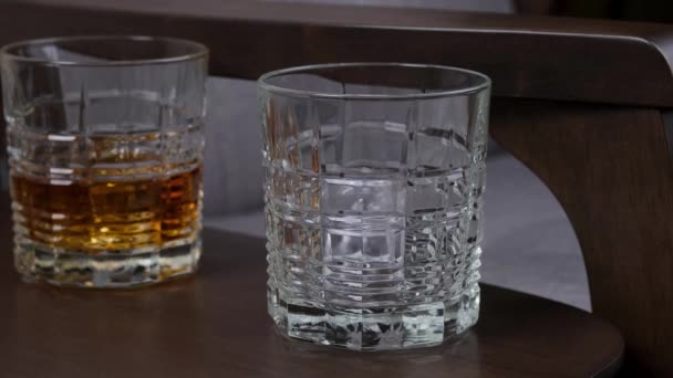 金色のウイスキーまたは木製の背景にボトルからガラスに注ぐ氷のキューブとコニャック — ストック動画