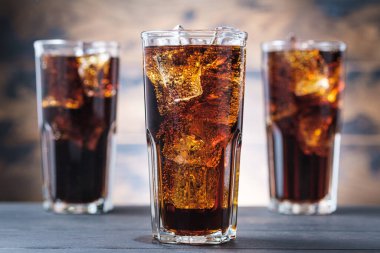 Three cola glass with ice cubes and bubbles. Cold sweet drink on wooden background clipart