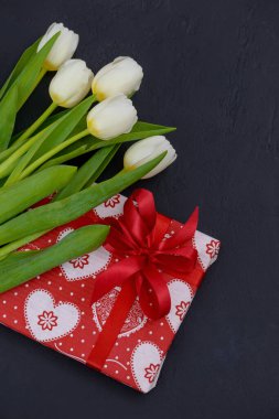 Beyaz laleler ve siyah arka planda kalp izi olan kırmızı hediye.