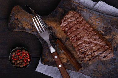 Kesme tahtasında çatal ve bıçakla ızgara biftek. Pişmiş yemek.