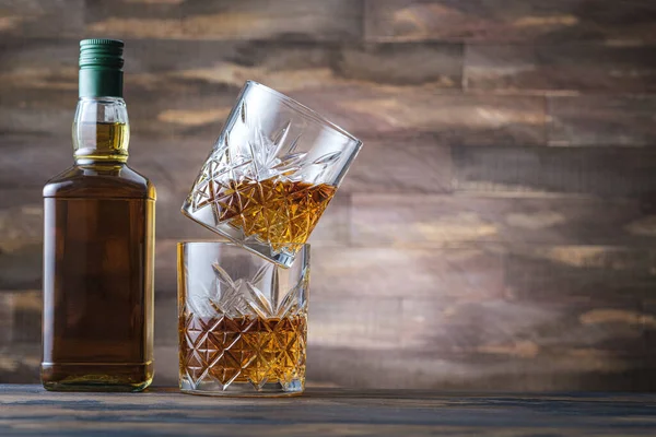 Bottle whiskey and two glass with bourbon or scotch. Rum or brandy on wooden background