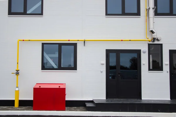 Yelow natural gas pipe, stainless steel flue pipe and red fire box installed in front of the modern building