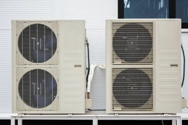 Close-up photo of two outdoor units of air conditioners standing on the ground in front of facade of the modern building — Stock Photo, Image