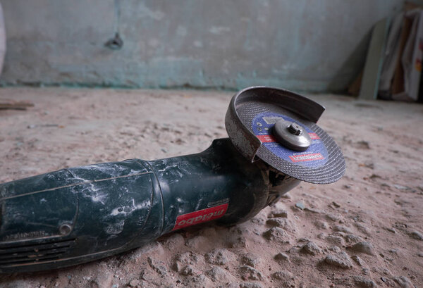 Side grinder on a floor in front of a dirty wall.