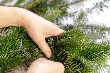 Bir kadının elleri köknar dallarından Noel çelengi yapar.