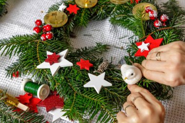 Bir kadının elleri köknar dallarından Noel çelengi süslüyor