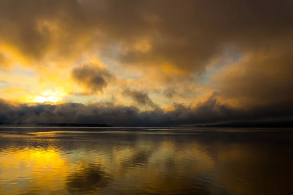 Salida del sol en el lago, reflejo del sol en el agua, con niebla y nubes en la mañana de verano — Foto de Stock
