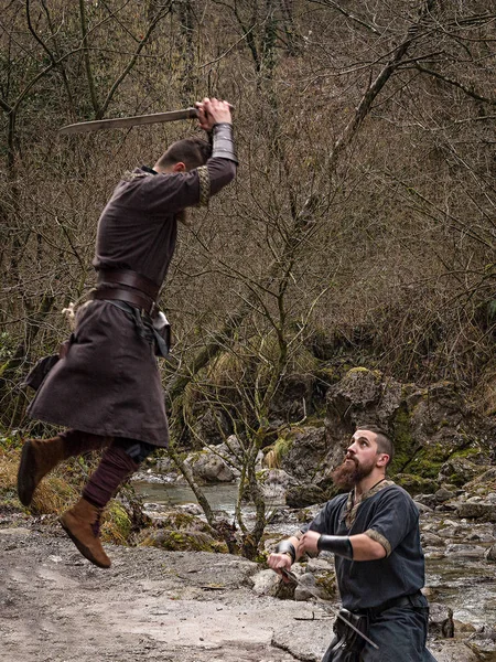 Two Viking warriors fight with the sword on the bank of the rive