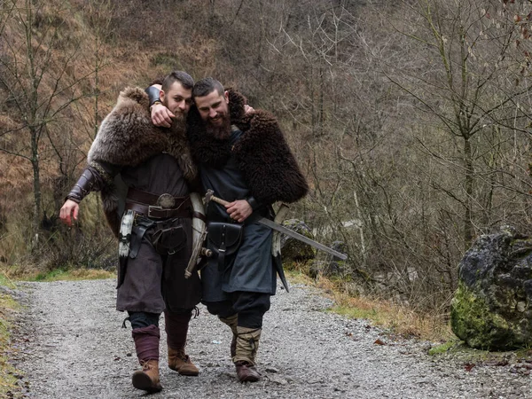 two Viking warriors walk hugged in the forest