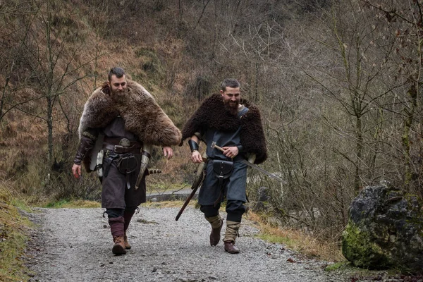 two Viking warriors walk on an ancient forest path