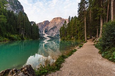 Toprak yol, bulutlu bir gökyüzü altında Braies Gölü boyunca uzanır. Arka planda Trentino Alto Adige 'deki Croda del Becco vardır.