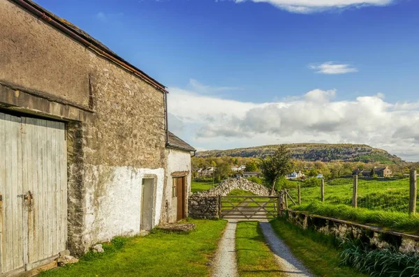 An old barn in Cumbria on a sunny day with a wooden gate and distant hills. — Stock Photo, Image