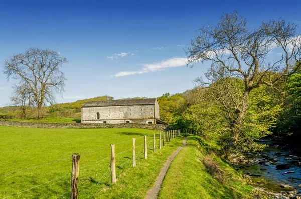 Eine abgelegene Scheune in grüner englischer Landschaft an einem Pfad entlang eines Flusses. — Stockfoto