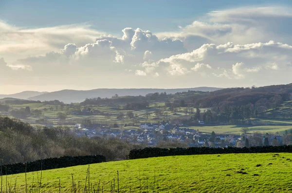 A green field with a village beyond and gowing cumulous clouds ont eh horizon — Stock Photo, Image