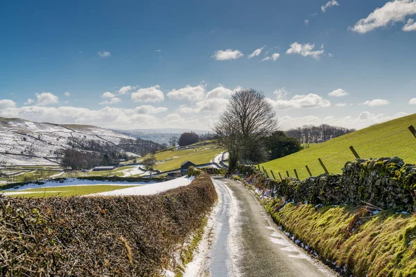 Een landweg leidt door sneeuw spattered landbouwgrond. — Stockfoto