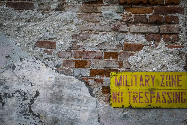 Do not cross the red plate on a yellow background hanging on a broken brick wall. a military zone and a sign that warns against a brick red fence.