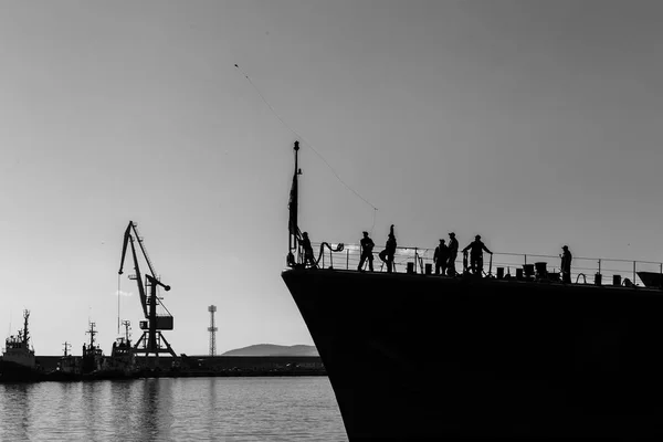セーラーは 軍用船の他の船員によって観測されたポートの重量とロープをスローします 黒と白の港を港に海軍の船を準備します — ストック写真