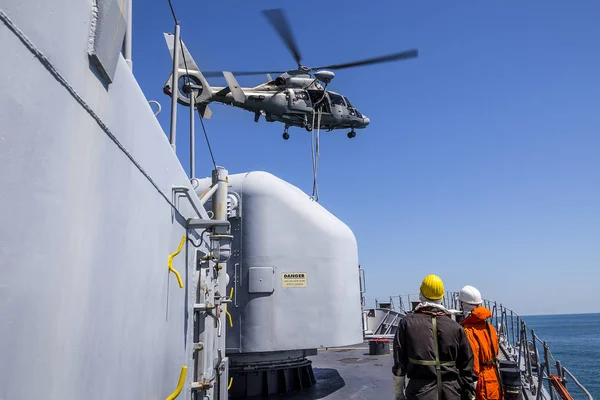 a helicopter provides the defense of a military warship. boarding of a vessel. sailors watch a helicopter dip over a ship. military drill and rescue operation.